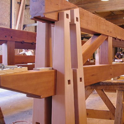Large dimension redwood beams are carved and then assembled into a unique structure. The assembly is shown in a workshop but will ultimately be the open beam structure for a celing in a custom home.